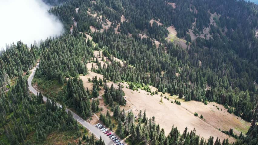 Mesmerizing aerial view of mist-covered mountains in Olympic National Park. Parked cars line the road, beckoning adventure in nature