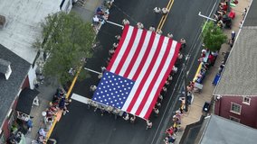 A small crowd watches a large Flag is carried past as part of the 4th July parade. Aerial view. - Powered by Shutterstock - Get 15% off with code: PIKWIZARD15