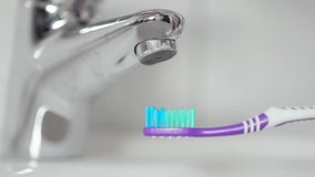 The faucet in the bathroom with running water and a toothbrush underneath it. Water is turned on and off in 4k slow-motion.  - Powered by Shutterstock - Get 15% off with code: PIKWIZARD15