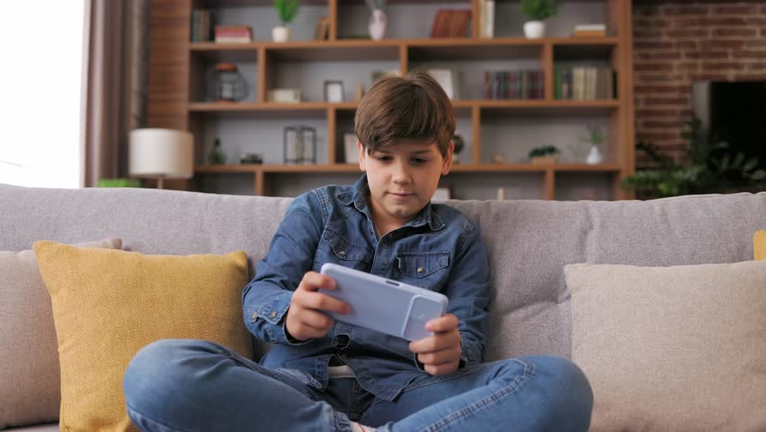 Teens and gaming addiction. Young boy playing video game on smartphone sitting on sofa at home. Cute teenager losing in car racing game on mobile phone. Spending time at home, leisure, relax. Royalty-Free Stock Footage #1106008859