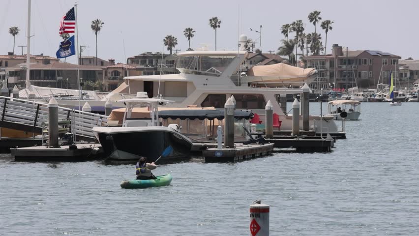 footage of gorgeous summer landscape with two women rowing a green kayak across the rippling ocean water with yachts and boats in the harbor at Horny Corner Beach in Long Beach California USA