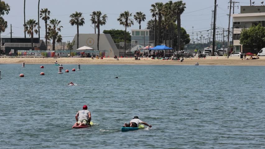 Footage of a beautiful summer landscape at Horny Corner Beach with two men on paddle boards on the ocean water and people relaxing on the beach in Long Beach California USA