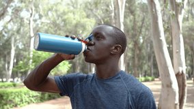 Video portrait of a male person of color in his thirties as he takes a refreshing break from his workout, sipping water from a blue water bottle in an outdoor park in Morocco, North Africa. 