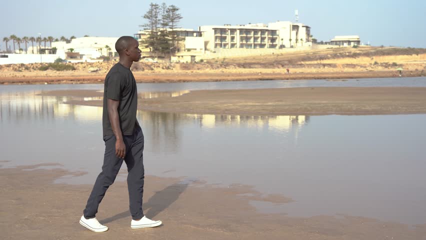 Portrait of a male person of color in his thirties as he gazes upon and enjoys the beauty of the beach on a sunny day in Morocco, North Africa.
