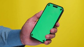 Man Holding a Smartphone with a Green Screen on a Yellow Background Close-Up, a Man Using a Phone With a Green Screen Mockup