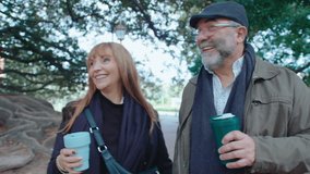 Happy senior couple holding travel mugs with coffee, smiling and having conversation, walking together in the park and enjoying the day outdoors - Powered by Shutterstock - Get 15% off with code: PIKWIZARD15
