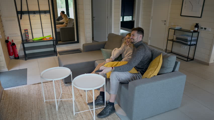 Relaxed loving couple watching TV switching channels with remote control in slow motion laughing. High angle view wide shot of happy Caucasian man and woman enjoying leisure together