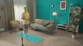 A man in sportswear is filming his home workout using a smartphone mounted on a tripod monopad. A man is jumping rope in the living room. Home fitness concept. Slow motion. HDR BT2020 HLG Material.
