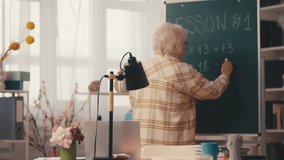 Senior female teacher writing math equations on chalkboard, explaining task