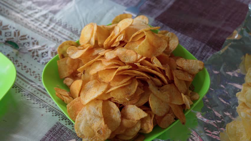 Close up of bowl with snacks on the table and hands of a young women taking chips. Girls enjoy junk food sitting in a gazebo in nature. Hands of people take chips from plastic bowl. Footage 4K 25FPS