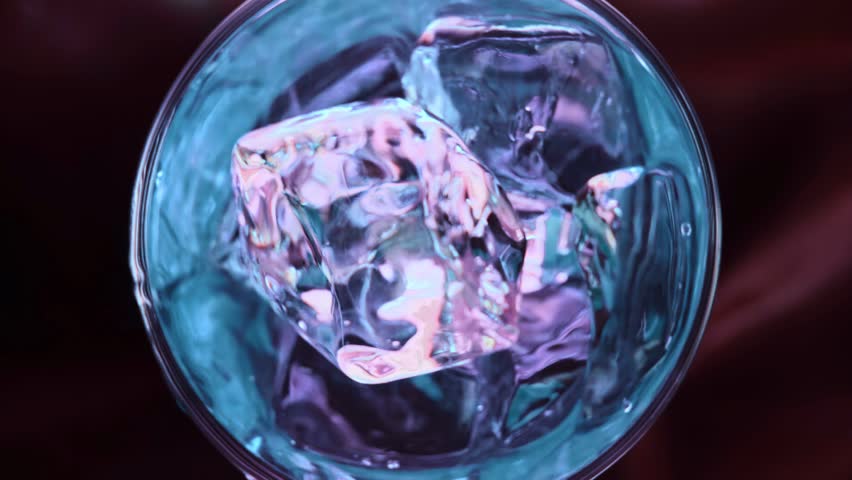 Slowmotion pours cocktail on spin ice cubes in turn glass.Super slow motion 1000fps top view on blue curacao cocktail on ice cubes in rotate glass.Slow motion turn ice cubes and blue alcohol cocktail Royalty-Free Stock Footage #1106036593
