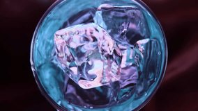 Slowmotion pours cocktail on spin ice cubes in turn glass.Super slow motion 1000fps top view on blue curacao cocktail on ice cubes in rotate glass.Slow motion turn ice cubes and blue alcohol cocktail - Powered by Shutterstock - Get 15% off with code: PIKWIZARD15