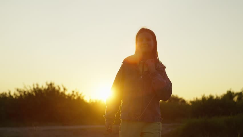 Happy cheerful teenage girl jumping with arms up at sunset. A carefree, interesting childhood. High quality 4k footage
