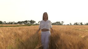 girl is walking along the wheat field nature slow motion video. Beautiful girl lifestyle in white dress running nature freedom happiness hands to the side on field at sunset light and the blue sky