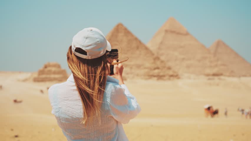 Tourist woman in takes photo on smartphone of Great Giza pyramids in Cairo Egypt enjoys attraction of world UNESCO ancient heritage, back view. Tourism travel wanderlust journey sightseeing concept. | Shutterstock HD Video #1106040387
