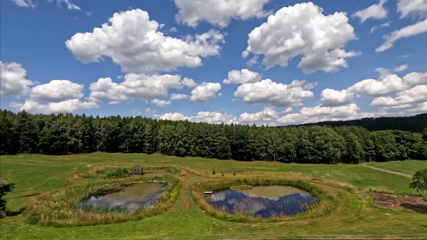 White fluffy clouds floating over two small ponds and reflecting on their surface - time lapse in motion