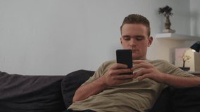 Young Man Sits on Couch and Stares at Phone, Concept Digital Connectivity, Social Media and Connectivity, Dependence on Technology  - Powered by Shutterstock - Get 15% off with code: PIKWIZARD15