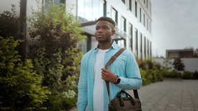 Young African American man with laptop in bag walks down street in summer morning. Guy looks at mobile phone and smiles reading funny message - Powered by Shutterstock - Get 15% off with code: PIKWIZARD15