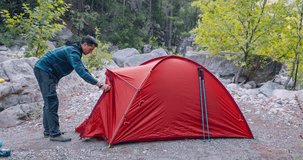 Timelapse video of a hiker man setting up a red camping tent in the woods