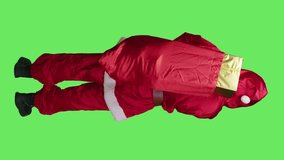 Vertical video Back view of father christmas looks around in studio, carrying big sack filled with presents boxes over full body greenscreen. Young man dressed as santa spreading xmas holiday spirit