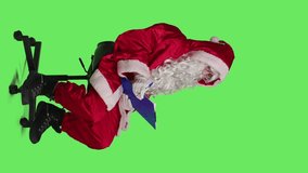 Vertical video Side view of winter character taking notes on papers, sitting on chair to write information on clipboard during christmas eve holiday. Santa claus man in cosplay posing over greenscreen