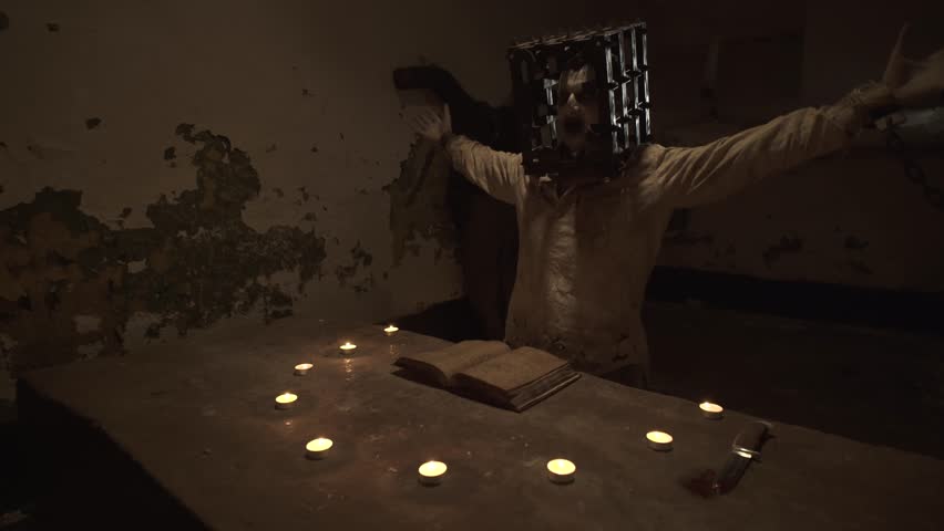 Ghost with cage on his head reading spells next to crucified body in basement.