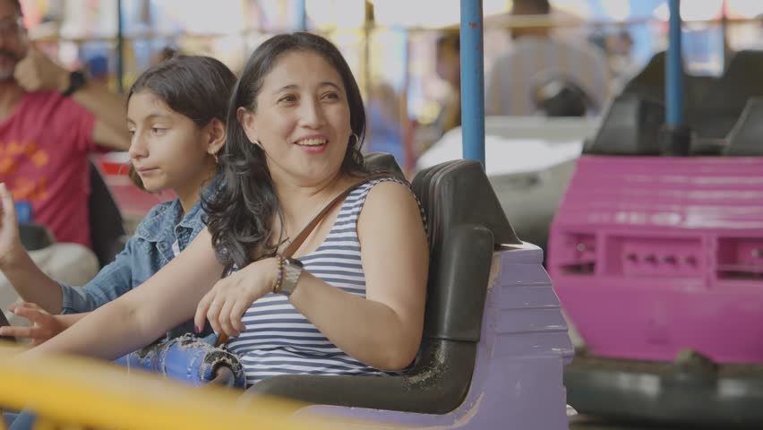 The family drives a bumper car at the amusement park, enjoying the ride. Royalty-Free Stock Footage #1106058733