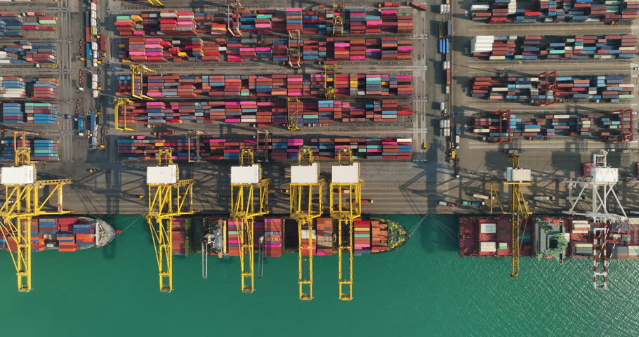 container ship and tugboat at commercial port loading and unloading cargo from container ship import and export by crane for distributing goods by trailers transported 4k video top view