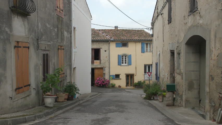 A quiet street in a small town in Routier in Southern France on a cloudy day. Old stone houses with wooden shutters line the street.
