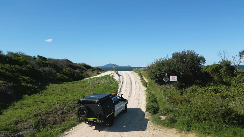 Aerial view of a Single Car driving along a long sandy beach. a beautiful blue sky day with the waves rolling in.