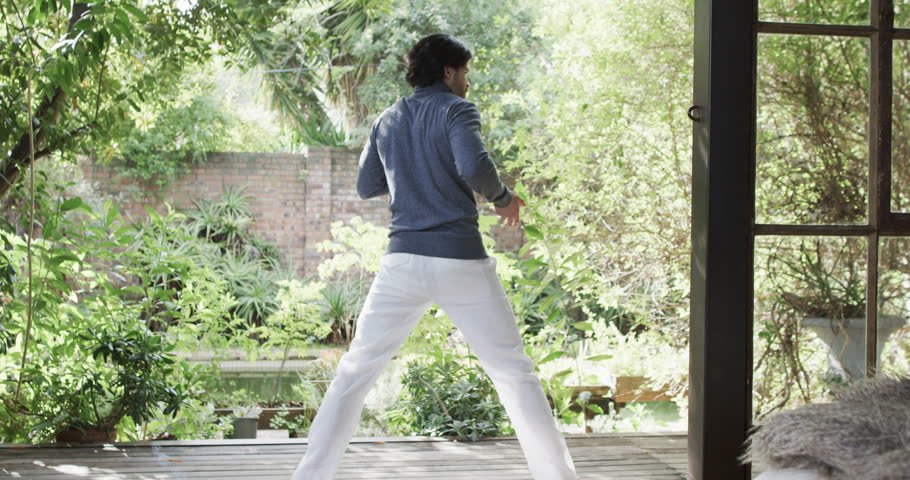 Caucasian man practicing yoga on terrace in sunny nature, slow motion. Healthy lifestyle, wellbeing in nature, exercise, fitness and domestic life, unaltered.
