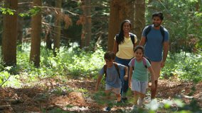 Family of four wearing backpacks walking towards camera through summer forest and exploring nature together with children running ahead as parents hold hands - shot in slow motion - Powered by Shutterstock - Get 15% off with code: PIKWIZARD15