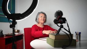 Senior female blogger recording video on professional camera and lighting setup.