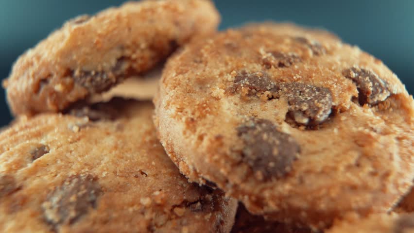 A macro close up cinematic shot of a plate full of crispy chocolate chip cookies, on a rotating stand, studio lighting, super slow motion, 120 fps, Full HD