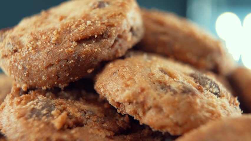 A macro close up cinematic shot of a plate full of crispy juicy chocolate chip cookies, on a rotating stand, studio lighting, super slow motion, 120 fps, Full HD video