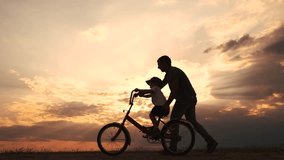 happy family in the park. father teaching son to ride a bike at sunset silhouette in the park. son child learning to ride a bike at sunset father helping son. child playing riding bike lifestyle - Powered by Shutterstock - Get 15% off with code: PIKWIZARD15