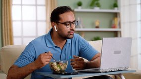 Happy indian man eating fruits salad while talking on online video call at home - concept of healthy eating, Video conference and Remote conversation