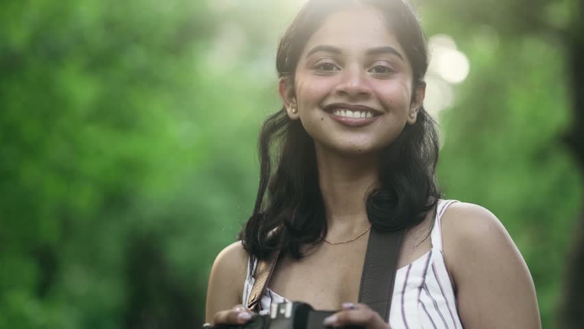 Portrait of pretty young indian woman photographer hold digital camera and looking at camera at green park Charming young tourist female taking pictures outdoors
