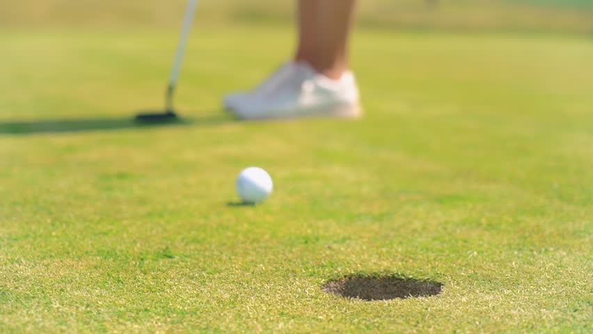 Mature woman playing golf. Golfer hitting golf shot and hammering a ball into the golf hole. Beautiful sunny andscape, with green hills and blue sky.