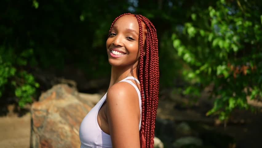 Outdoor portrait of natural Beautiful young African American woman long red braids hair style and perfect white teeth smile, posing in swimsuit at sunny summer day with green foliage beach background Royalty-Free Stock Footage #1106089089