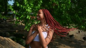 Outdoor portrait of natural Beautiful young African American woman long red braids hair style and perfect white teeth smile, posing in swimsuit at sunny summer day with green foliage beach background - Powered by Shutterstock - Get 15% off with code: PIKWIZARD15