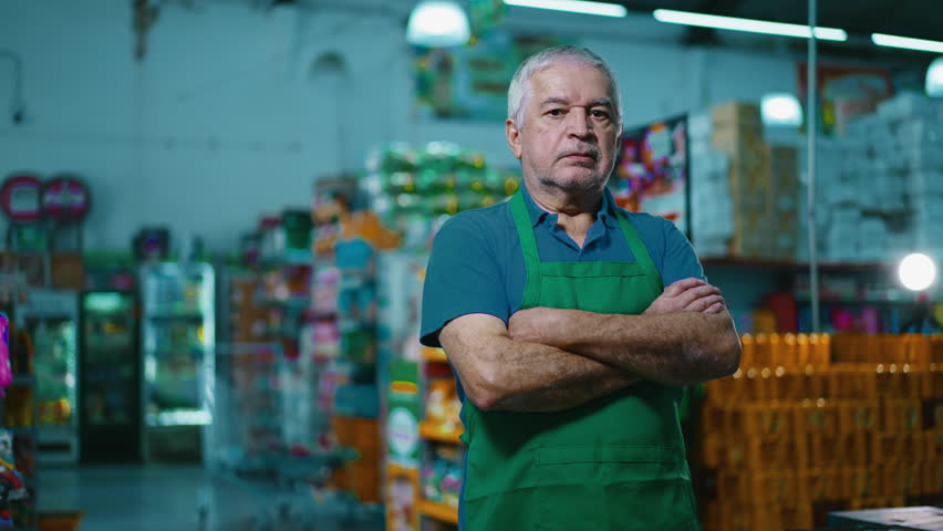 Serious small business owner with arms crossed standing inside Grocery Store chain. Concerned preoccupied expression of an older supermarket manager wearing apron Royalty-Free Stock Footage #1106089263