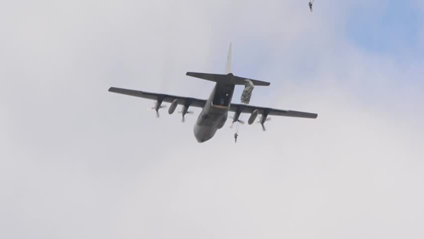 military paratroopers jumping from the rear hatch of a military transport plane