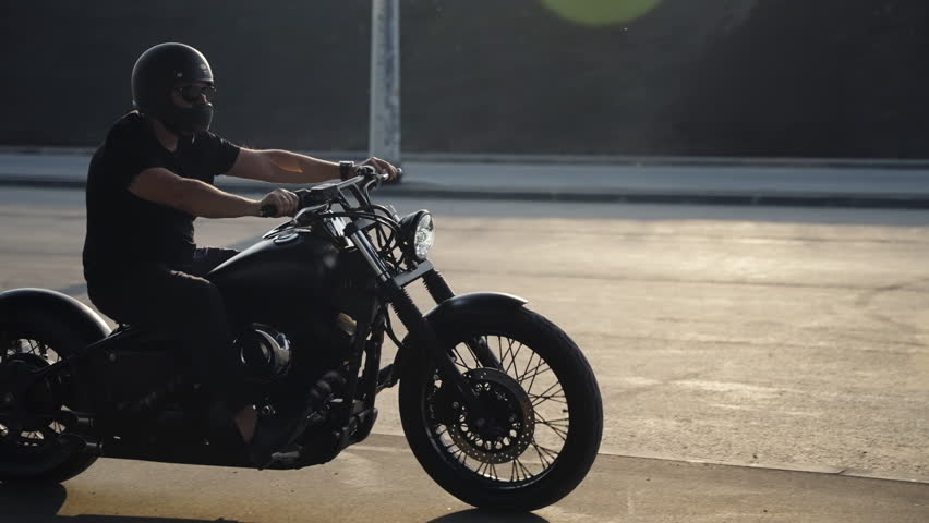 Brutal man rides his collectible bike. The shadow of the motorcycle is reflected on the asphalt. Active bike riding. Brutal biker in black clothes. Fast riding on a motorcycle.