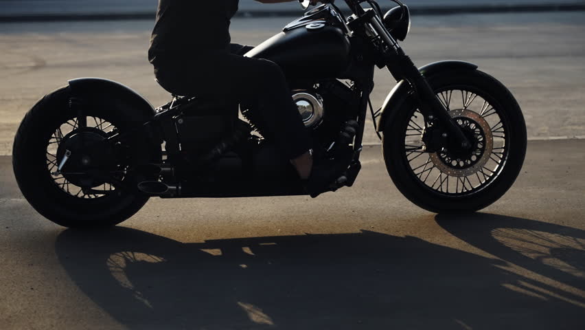 Motorcycle in profile. A man in a protective helmet. A motorcycle rides on asphalt in the parking lot. Biker with glasses. Chrome parts.