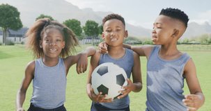 Video portrait of three happy african american children holding football in school field. Education, childhood, inclusivity, health, sport, elementary school and learning concept.