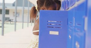 Video portrait of happy african american schoolgirl using locker at school. Education, childhood, inclusivity, elementary school and learning concept.