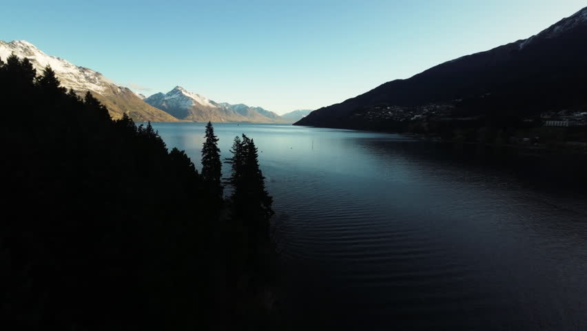 Aerial cinematic shot of snow-capped mountains overlooking a lake in Queenstown