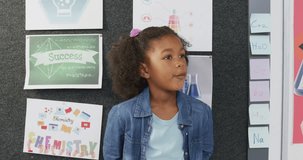 Video portrait of happy biracial schoolgirl smiling in school classroom. Education, childhood, inclusivity, elementary school and learning concept.