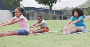 Video of diverse schoolgirls and schoolboy practicing yoga stretching in outdoor class, copy space. Education, childhood, inclusivity, health, elementary school and learning concept.